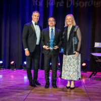 Dr. Richard Chang of Children’s Hospital of Orange County Metabolic Lab, standing in for award winner Dr. Jose Abdenur, with host Peter Alexander and NORD CEO Pamela Gavin